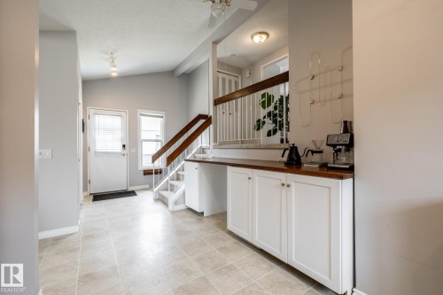 Side entryway featuring tile flooring, a white door with an integrated window blind, a single window, a staircase with wood handrails, beside the kitchen with built-in white cabinetry with a wood countertop - 3608 16A Avenue, Edmonton, AB - Indoor Photo Showing Other Room