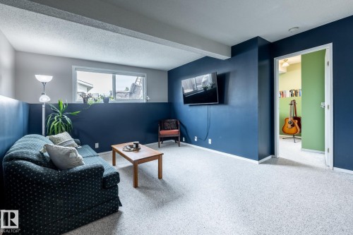 Interior room featuring light-colored carpeting, a two-tone wall treatment with a dark blue lower section and lighter upper section, and a mounted flat-screen television - 3608 16A Avenue, Edmonton, AB - Indoor