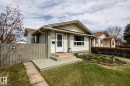Exterior of the home featuring light-colored siding with contrasting trim, a front porch with steps and a landing, a manicured lawn, a fence, and a landscaped garden bed - 3608 16A Avenue, Edmonton, AB  - Outdoor 