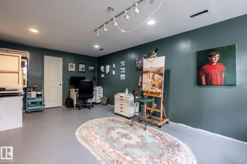 Spacious room featuring dark teal walls, recessed lighting, track lighting, a white interior door, and light gray flooring, currently in use as an art studio - 3608 16A Avenue, Edmonton, AB - Indoor Photo Showing Other Room