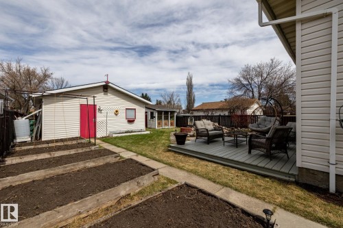 Backyard featuring a composite deck, a detached garage with red access door, and multiple raised garden beds - 3608 16A Avenue, Edmonton, AB - Outdoor With Exterior