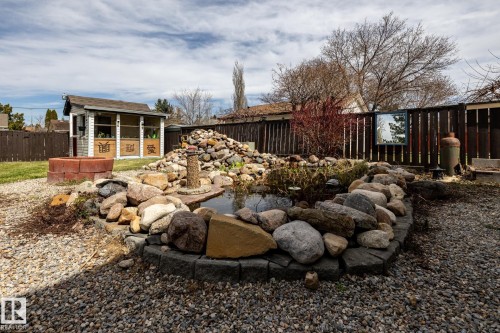 Backyard featuring a rock-lined koi pond with a central water feature, a shingled garden shed with screened panels, a red brick fire pit, and a dark wood privacy fence - 3608 16A Avenue, Edmonton, AB - Outdoor