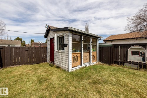 Detached garden shed with white siding and a brown shingle roof, featuring a red entry door, a window with a dark planter, and a sunroom extension with large glass panels - suitable as a little greenhouse or potting shed - 3608 16A Avenue, Edmonton, AB - Outdoor