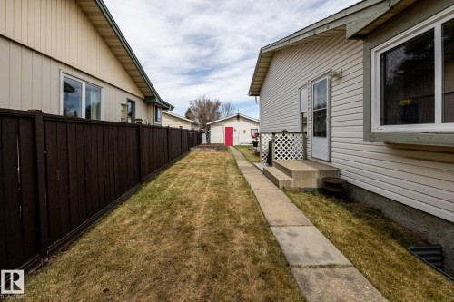 Side yard featuring a concrete walkway, mature lawn, and dark wood privacy fence looking towards the rear garage - 3608 16A Avenue, Edmonton, AB - Outdoor With Exterior