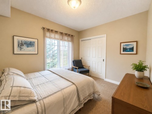 Neutral-toned bedroom featuring a large window with white muntins and sheer curtains, light beige walls, and tan carpet flooring - 301 9803 96A Street, Edmonton, AB - Indoor Photo Showing Bedroom