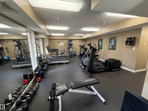 Dedicated fitness area featuring durable rubber flooring, mirrored wall, multiple cardio machines, weight equipment, and recessed lighting - 301 9803 96A Street, Edmonton, AB - Indoor Photo Showing Gym Room