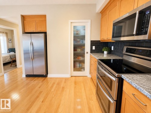 Kitchen featuring wood-finish flooring, stainless steel appliances, light wood cabinetry, stone countertops, and a dark tile backsplash - 301 9803 96A Street, Edmonton, AB - Indoor Photo Showing Kitchen