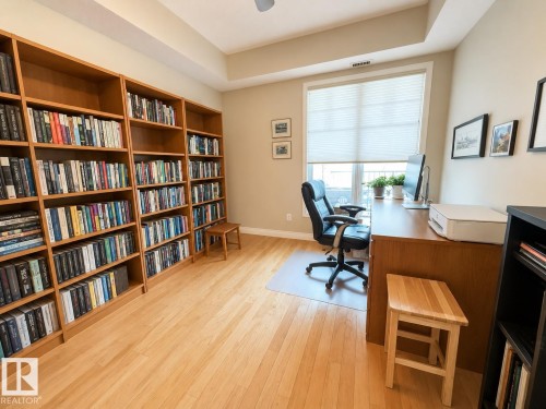 Built-in wood-finish shelving, light wood-finish flooring, and a large window with privacy blinds - 301 9803 96A Street, Edmonton, AB - Indoor Photo Showing Office