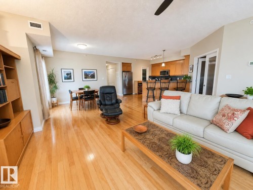 Open-concept living space featuring wood-finish flooring throughout, a dining area with a rectangular table, and a kitchen with an eat-at counter - 301 9803 96A Street, Edmonton, AB - Indoor Photo Showing Living Room