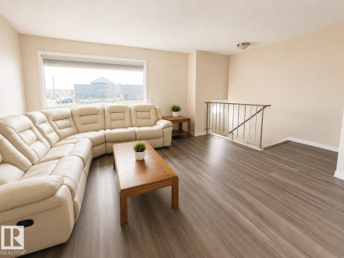 Expansive living area featuring wood-finish flooring, a large picture window, a neutral color palette, and a metal stair railing - 5712 101 Avenue, Edmonton, AB - Indoor Photo Showing Living Room