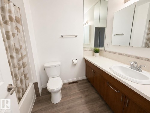 Bathroom featuring wood-finish flooring, a white porcelain toilet, and a bathtub with a shower - 5712 101 Avenue, Edmonton, AB - Indoor Photo Showing Bathroom
