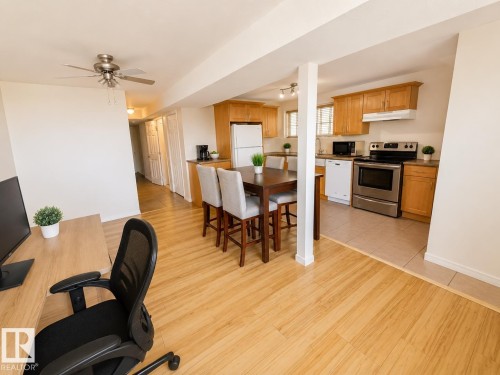 Open-concept living space featuring wood-finish flooring, a ceiling fan, and a kitchen with wood cabinetry, stainless steel appliances, and tile flooring - 5712 101 Avenue, Edmonton, AB - Indoor