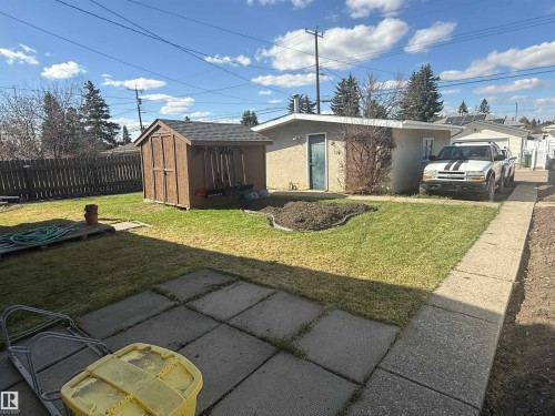Expansive backyard featuring a manicured lawn, a wood-finish shed with a shingled roof, a paved patio area, and a concrete pathway - 5712 101 Avenue, Edmonton, AB - Outdoor