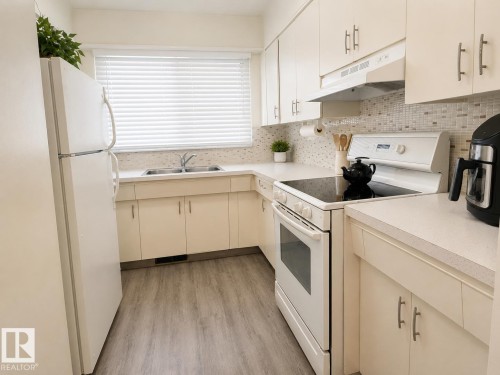 Kitchen featuring cream-colored cabinetry with brushed nickel hardware, white appliances, and light wood-finish flooring - 5712 101 Avenue, Edmonton, AB - Indoor Photo Showing Kitchen With Double Sink
