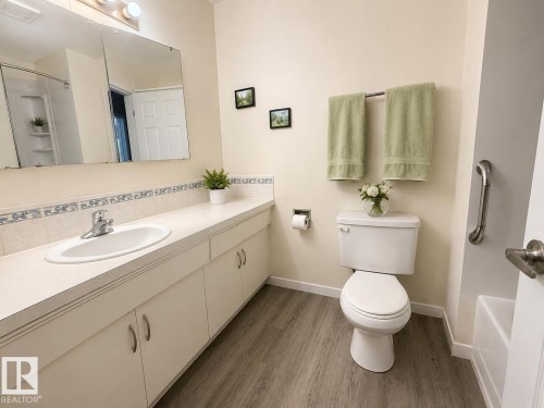 Bathroom featuring a spacious vanity with integrated sink, white cabinetry, wood-finish flooring, and a shower with built-in shelving - 5712 101 Avenue, Edmonton, AB - Indoor Photo Showing Bathroom