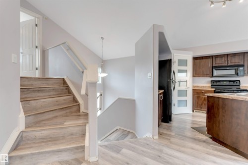 Staircase with wood-finish flooring and white railings, complemented by a contemporary pendant light fixture - 123 Rue Masson, Beaumont, AB - Indoor Photo Showing Kitchen