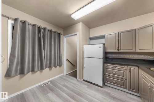 Kitchen area featuring wood-finish flooring, neutral cabinetry, dark countertops, and a tiled backsplash - 11414 85 Street, Edmonton, AB - Indoor Photo Showing Kitchen