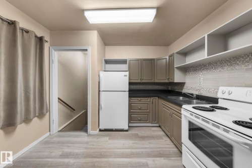 Kitchen featuring wood-finish flooring, L-shaped cabinetry with dark countertops, white appliance suite, and a decorative tile backsplash - 11414 85 Street, Edmonton, AB - Indoor Photo Showing Kitchen With Double Sink