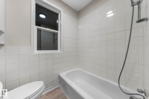 Bathroom featuring a white bathtub, ceramic wall tiling, and wood-finish flooring - 11414 85 Street, Edmonton, AB - Indoor Photo Showing Bathroom