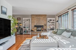Living area featuring a stone accent wall, wood-finish flooring, and ample natural light from multiple windows - 