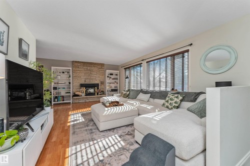 Living area featuring wood-finish flooring, a stone-clad fireplace, and twin built-in shelving units - 49 Ash Crescent, St. Albert, AB - Indoor Photo Showing Living Room With Fireplace
