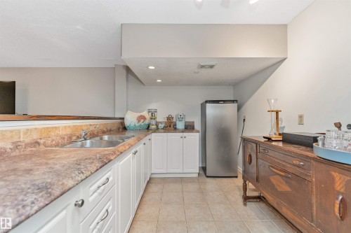 Lower level kitchenette featuring white cabinetry, a double basin stainless steel sink, and patterned countertops - 49 Ash Crescent, St. Albert, AB - Indoor Photo Showing Kitchen With Double Sink