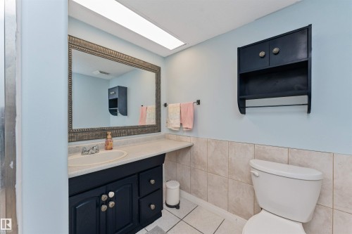Bathroom featuring a vanity with an integrated sink, a large framed mirror, a wall-mounted storage cabinet, and tiled wainscoting - 49 Ash Crescent, St. Albert, AB - Indoor Photo Showing Bathroom