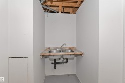 Utility sink area featuring a dual stainless steel sink, a patterned countertop, and exposed overhead joists - 