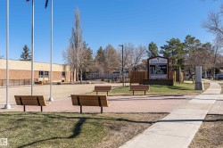 Paved courtyard featuring multiple park benches, a brick-faced building, and mature trees - 