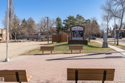 Brick paver walkway with wood benches, surrounded by landscaped green spaces and mature trees - 
