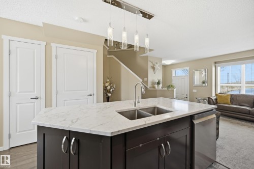 Kitchen island with a light-toned countertop, double basin sink, and pendant lighting - 481 Sheppard Boulevard, Leduc, AB - Indoor Photo Showing Kitchen With Double Sink