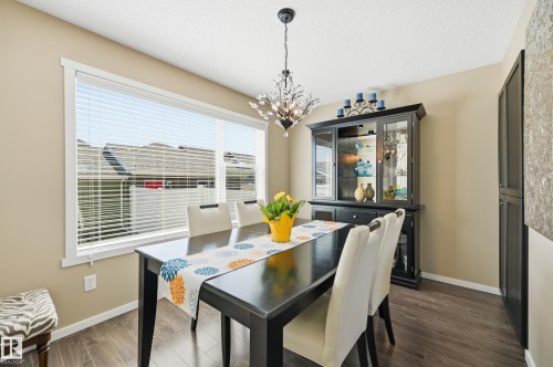 Dining area featuring wood-finish flooring, a large window with white blinds, and a decorative crystal chandelier - 481 Sheppard Boulevard, Leduc, AB - Indoor Photo Showing Dining Room