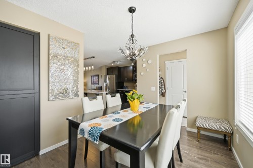 Dining area featuring wood-finish flooring, a contemporary chandelier, and a large window with blinds - 481 Sheppard Boulevard, Leduc, AB - Indoor Photo Showing Dining Room