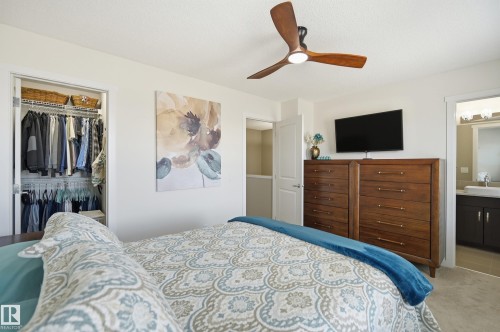 Bright bedroom with a modern ceiling fan, large closet with organized shelving, and a nearby bathroom entry featuring a vanity with a rectangular vessel sink - 481 Sheppard Boulevard, Leduc, AB - Indoor Photo Showing Bedroom