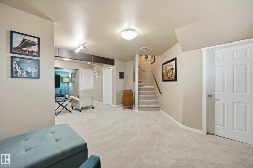 Spacious carpeted area with neutral wall tones, a paneled door, and a staircase with wood railing - 481 Sheppard Boulevard, Leduc, AB - Indoor Photo Showing Other Room
