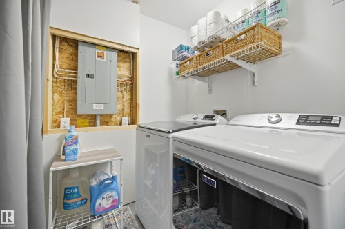 Dedicated utility area featuring a circuit breaker panel, two white appliances, and wall-mounted wire shelving - 481 Sheppard Boulevard, Leduc, AB - Indoor Photo Showing Laundry Room