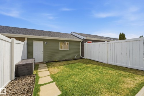 Enclosed backyard featuring green siding, a white service door, a window, a partial pathway of stepping stones, and white perimeter fencing - 481 Sheppard Boulevard, Leduc, AB - Outdoor With Exterior