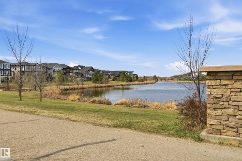 Expansive waterfront property featuring a tranquil lake, residential homes, green spaces, and a stone wall accent - 481 Sheppard Boulevard, Leduc, AB - Outdoor With View