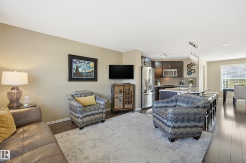 Open-concept living area featuring rich wood-finish flooring, a contemporary kitchen with stainless steel appliances, a spacious island with seating, and a formal dining area - 481 Sheppard Boulevard, Leduc, AB - Indoor