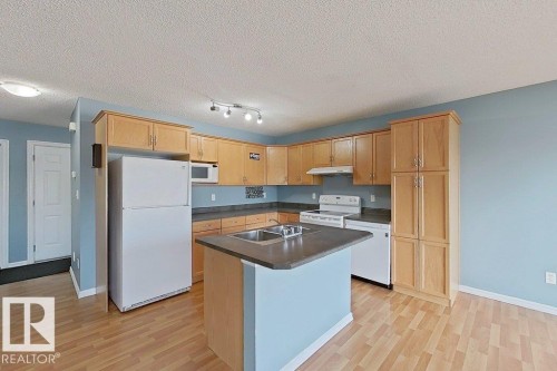 The kitchen features wood cabinetry, light blue walls, and light-toned flooring - 3347 24 Avenue, Edmonton, AB - Indoor Photo Showing Kitchen With Double Sink
