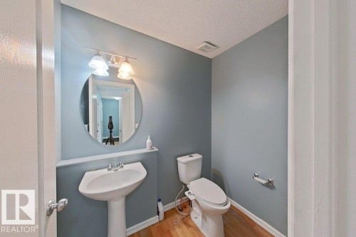 Well-appointed bathroom featuring a pedestal sink, an oval mirror, and a toilet - 3347 24 Avenue, Edmonton, AB - Indoor Photo Showing Bathroom