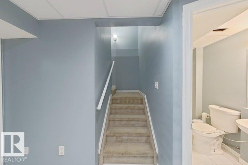 The property features a staircase with carpeted treads and a white handrail, illuminated by a wall sconce - 3347 24 Avenue, Edmonton, AB - Indoor Photo Showing Bathroom