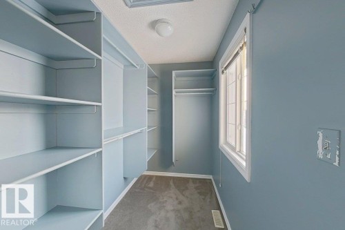 This walk-in closet features extensive shelving and hanging rods for ample storage, complemented by a window for natural light and a ceiling-mounted light fixture - 3347 24 Avenue, Edmonton, AB - Indoor