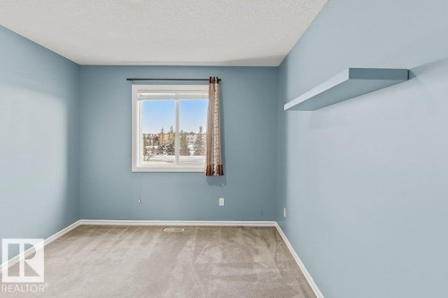 This room features light blue walls, neutral carpeting, and a window providing views of the surrounding area - 3347 24 Avenue, Edmonton, AB - Indoor Photo Showing Other Room