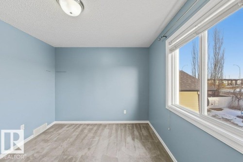 This room features light blue walls, gray carpet, and a large window providing natural light - 3347 24 Avenue, Edmonton, AB - Indoor Photo Showing Other Room