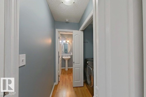 Hallway with light blue walls and hardwood floors, leading to a bathroom with a pedestal sink and a laundry area - 3347 24 Avenue, Edmonton, AB - Indoor