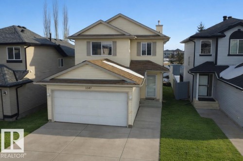 The property features an attached garage with a white garage door, a paved driveway, and a front lawn - 3347 24 Avenue, Edmonton, AB - Outdoor With Facade