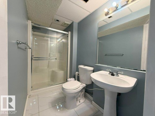 Bathroom featuring a shower with a sliding glass door, a toilet, a pedestal sink, and a mirror with an overhead light fixture - 3347 24 Avenue, Edmonton, AB - Indoor Photo Showing Bathroom