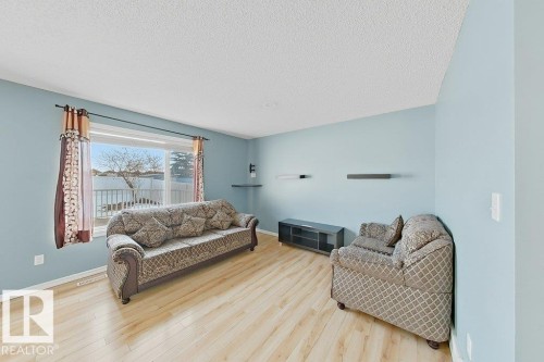 Living room featuring light blue walls, light-toned wooden flooring, and a large window with a view of a body of water - 3347 24 Avenue, Edmonton, AB - Indoor Photo Showing Living Room