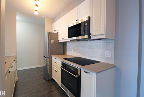 Kitchen featuring white shaker-style cabinetry, stainless steel appliances, a subway tile backsplash, light-toned countertops, and wood-finish flooring - 901 10160 116 Street, Edmonton, AB - Indoor Photo Showing Kitchen